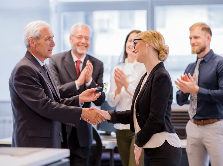 Een manager overhandigt een medewerker een cadeaukaart onder applaus van het team